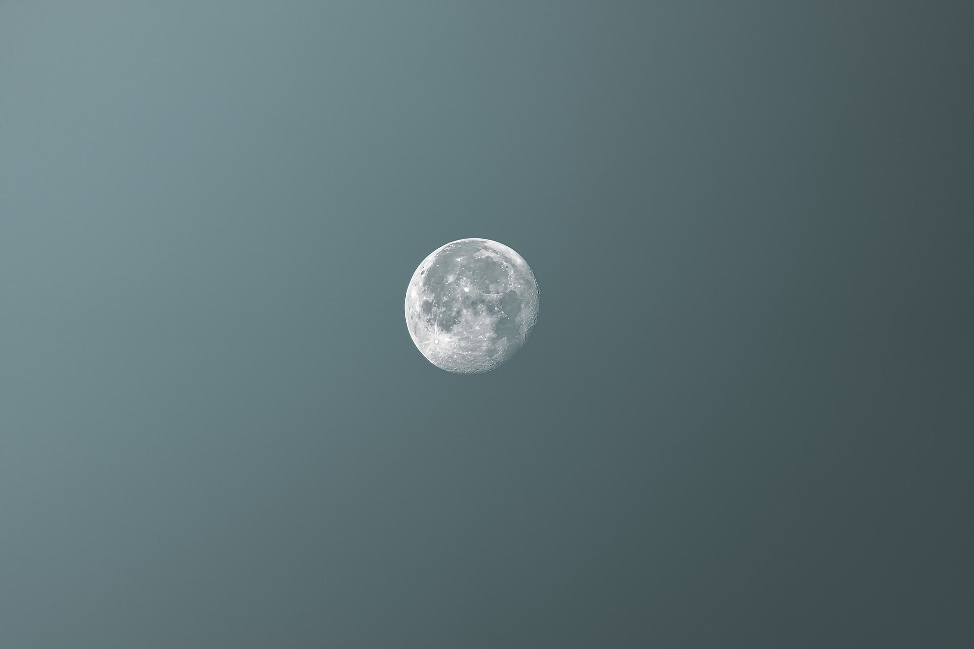 (Moon) A near-full moon floats against a moody blue-grey sky, its craters and surface detail rendered with striking clarity &mdash; a testament to the Sony RX10 V's reach at the long end of its zoom range.