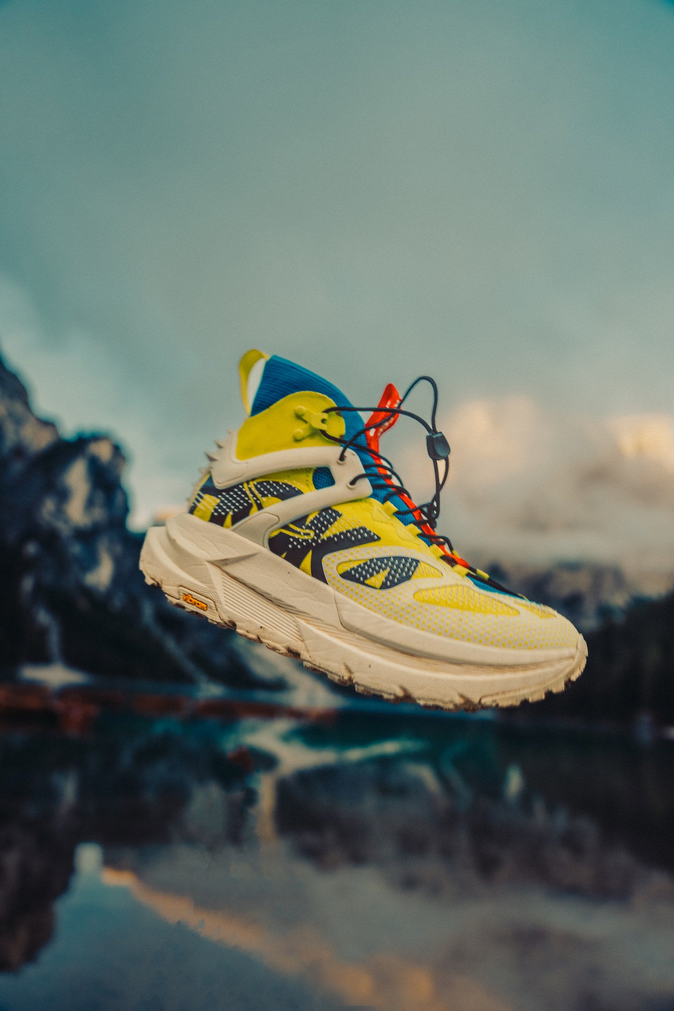 Yellow, white and blue sneaker levitating in air in front of mountain scene
