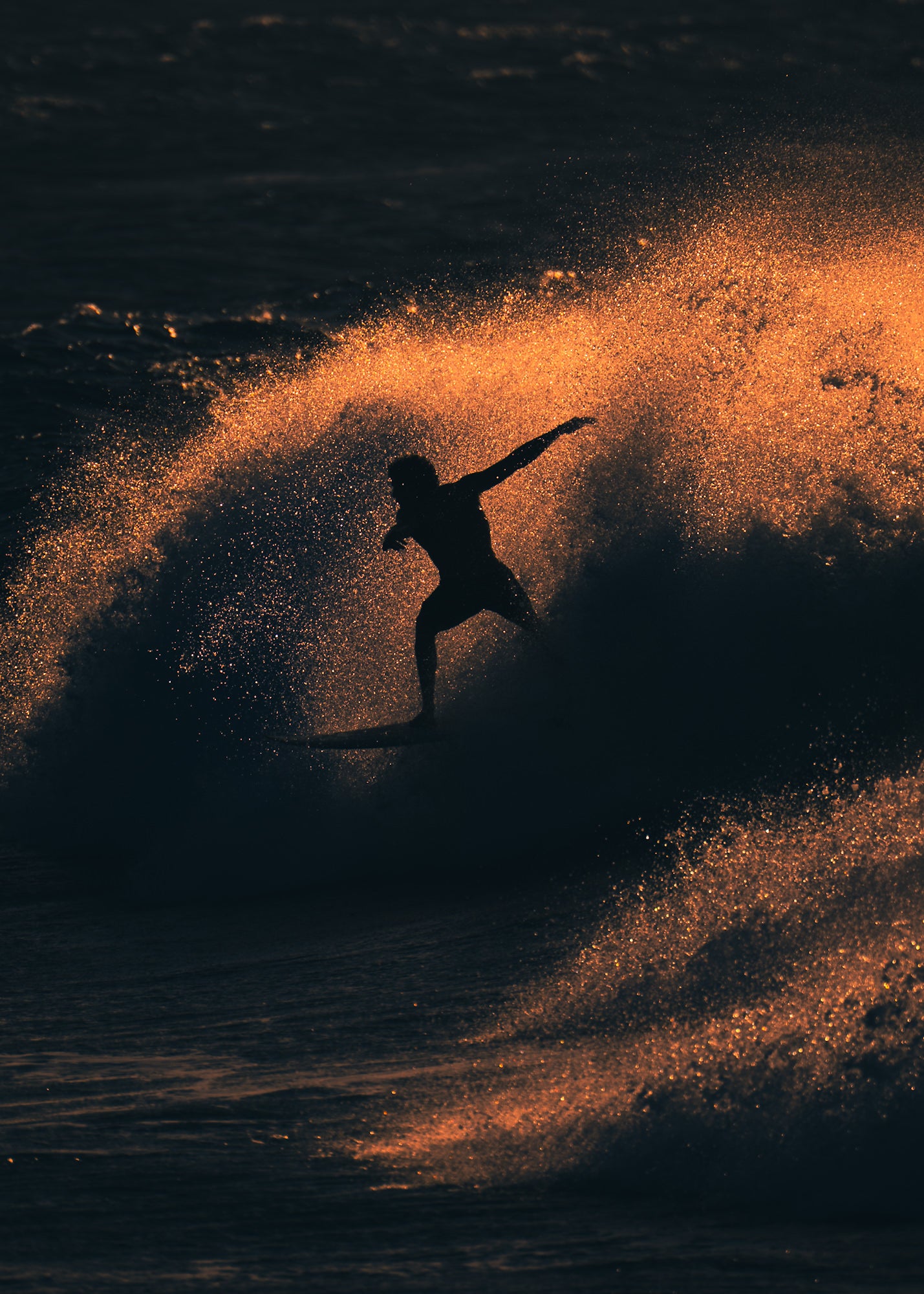 A surfer silhouetted against an explosive burst of golden spray executes a powerful carving turn as the wave erupts around them at sunset.