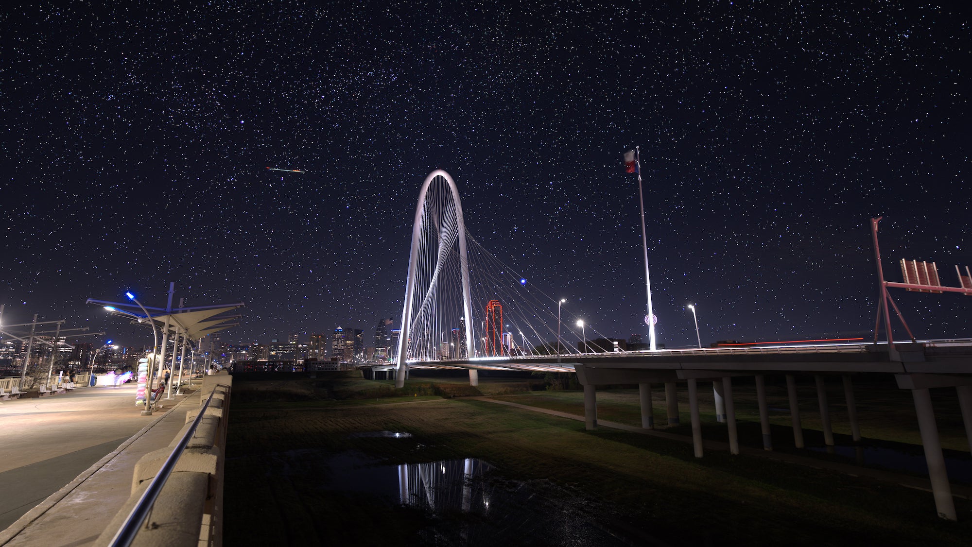 Margaret Hunt Hill Bridge in Dallas at night with the Texas flag and downtown skyline beneath a starry sky.