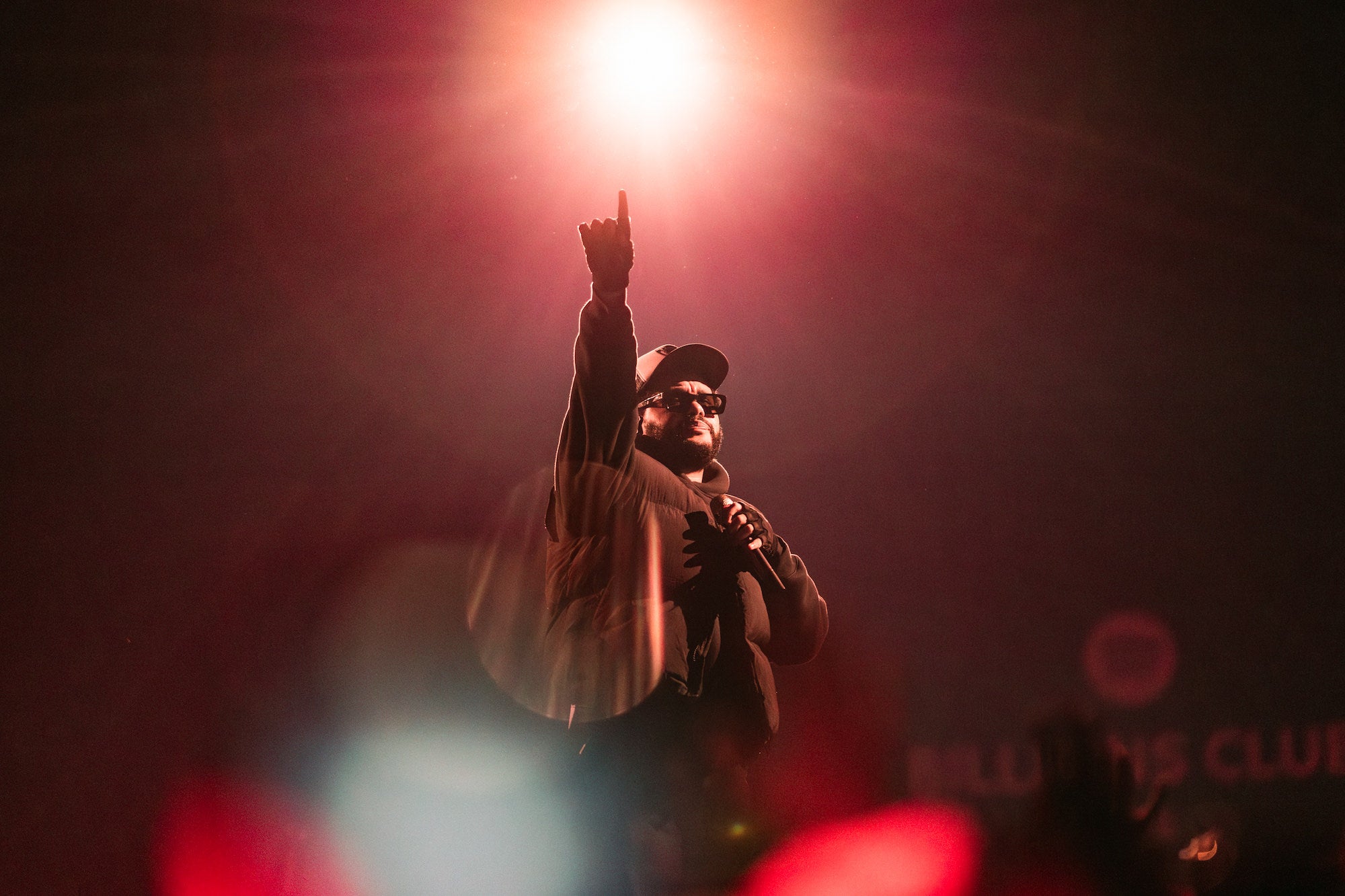 Performer points toward a bright stage light, bathed in warm red glow.