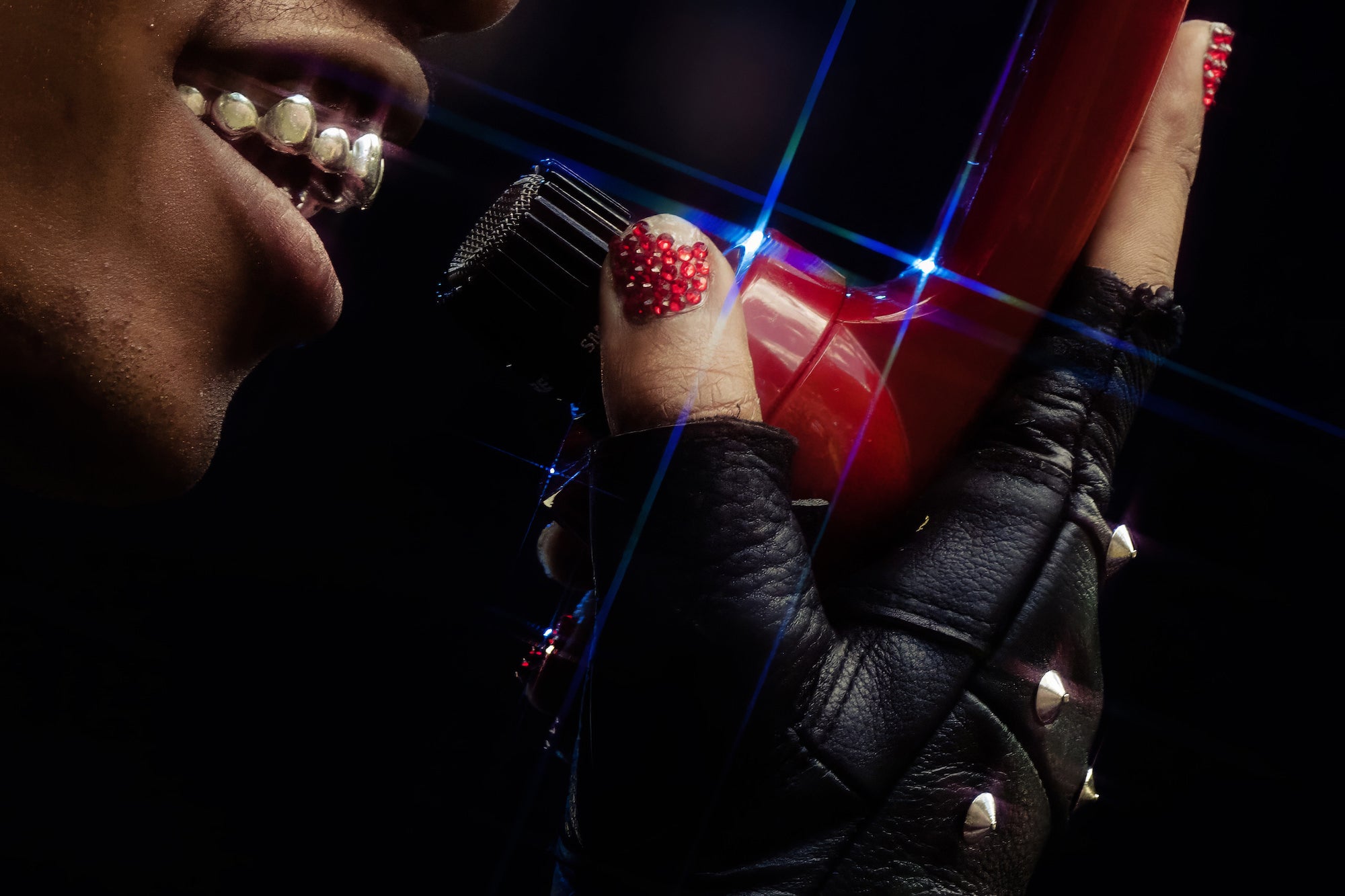 Extreme close-up of studded glove holding mic; glittered nail art sparkling.
