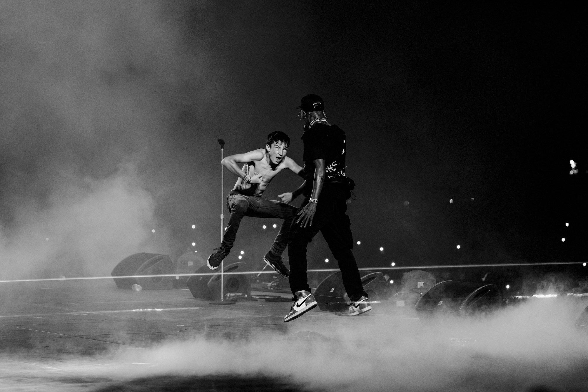 Two performers mid-jump on smoky stage, black-and-white action moment.