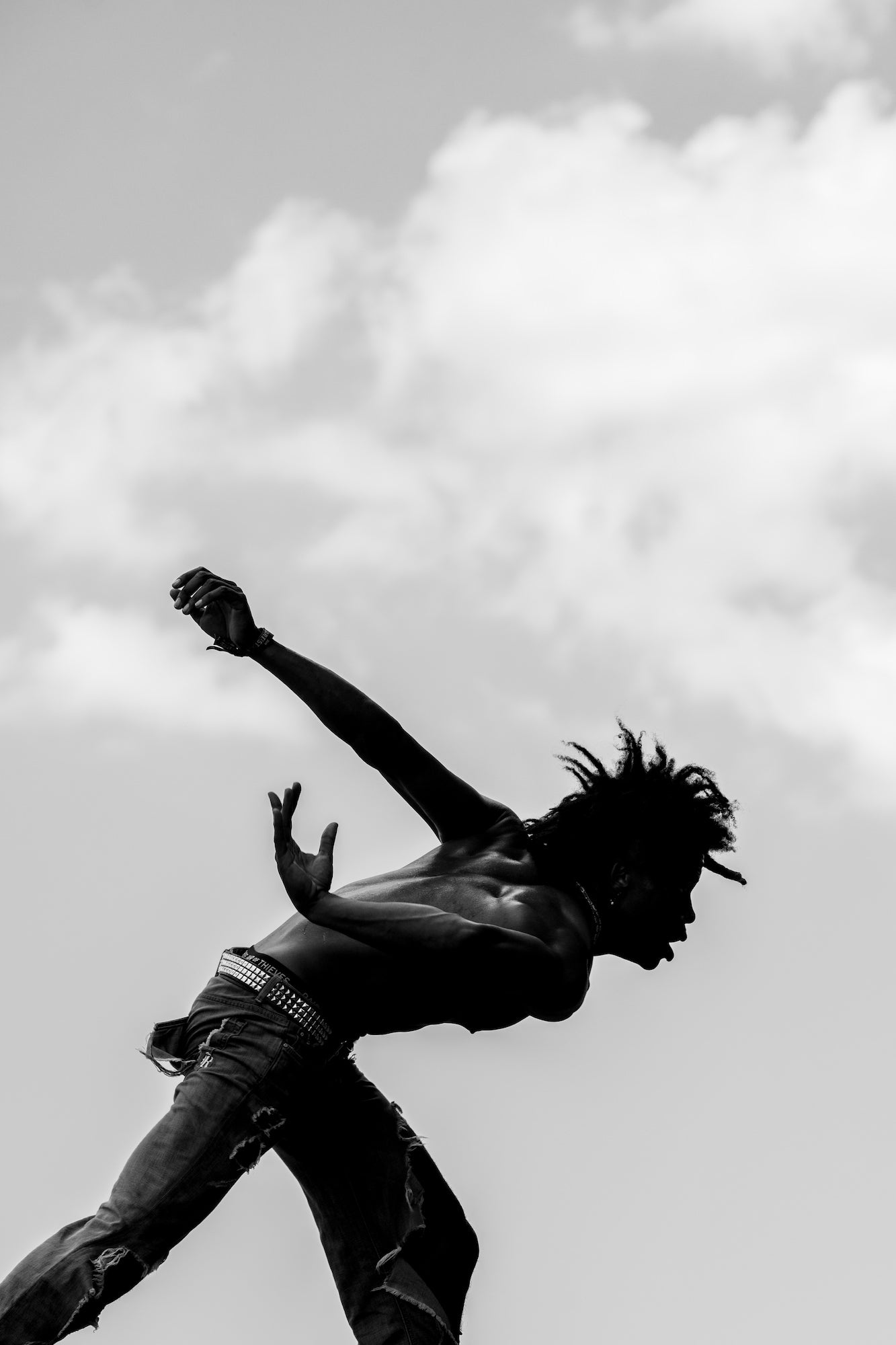 Silhouetted dancer mid-leap against cloudy sky, arms and torso arched.