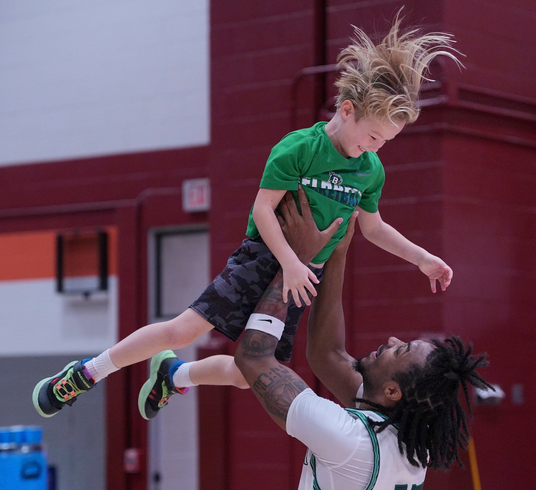 Player lifts smiling child in green shirt during postgame moment