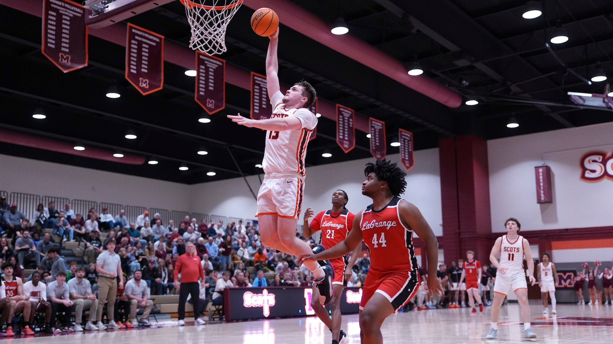 Forward in white rises for layup as crowd watches