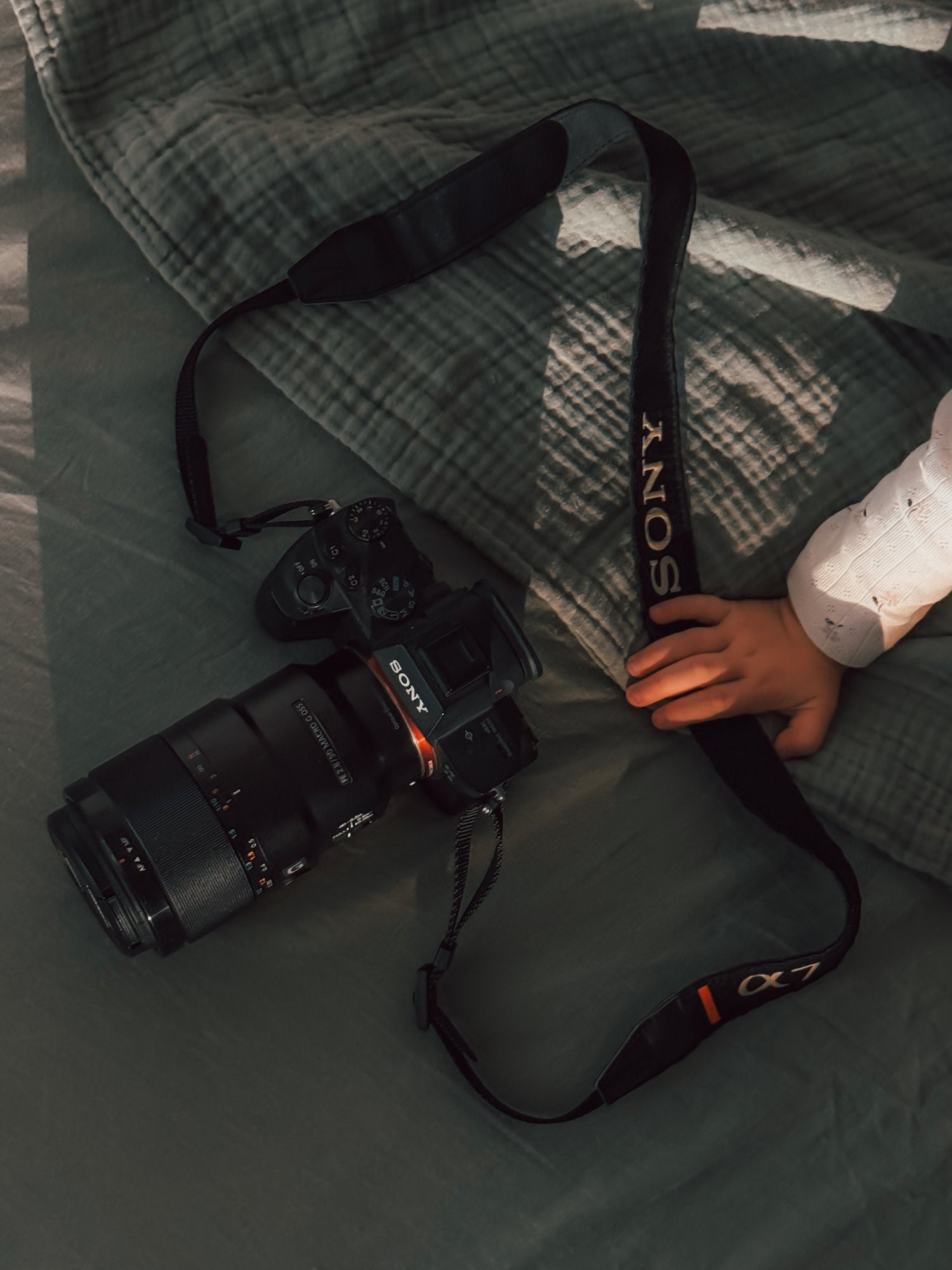 Sony Alpha 7 III camera with telephoto lens on a quilted bed beside a small hand.