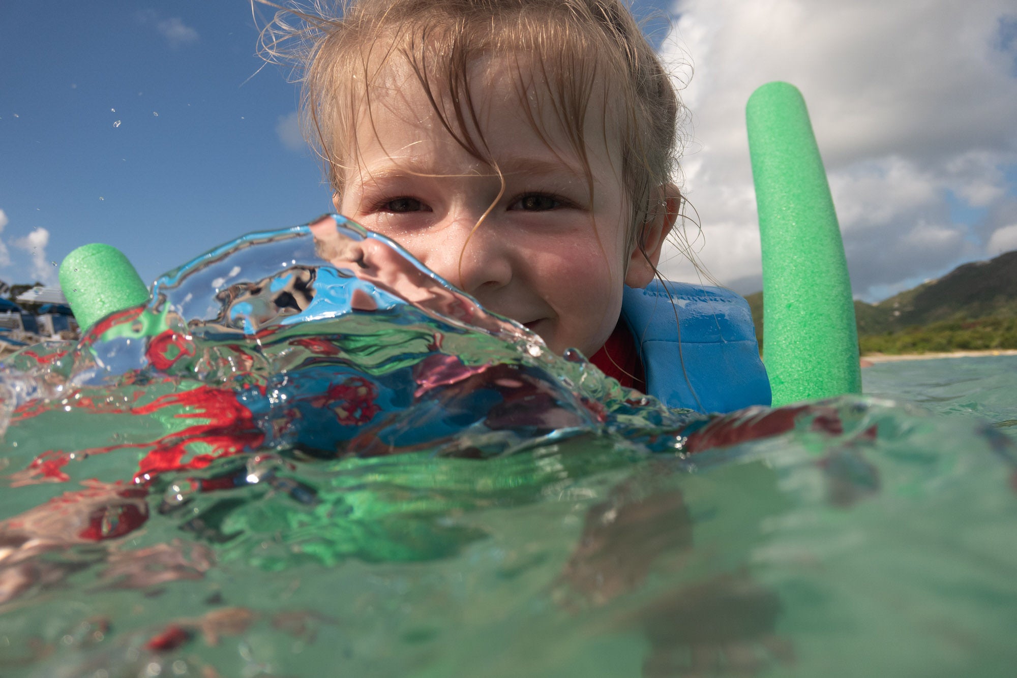 Child swimming with float aids; water splashes across the lens near shore.