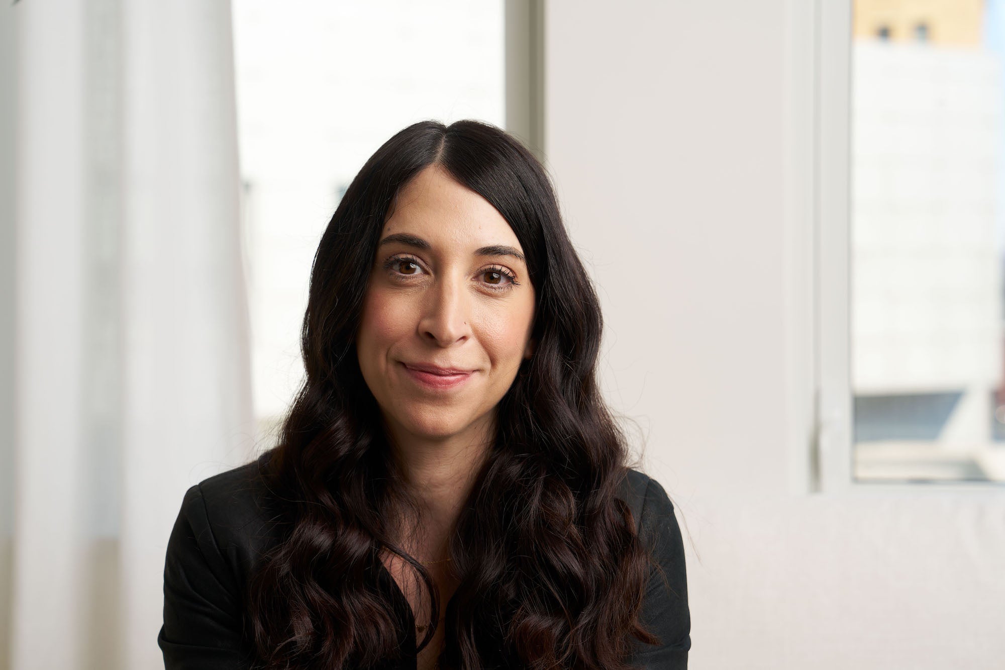 Natural-light headshot of a woman by a bright window, soft background and gentle smile.