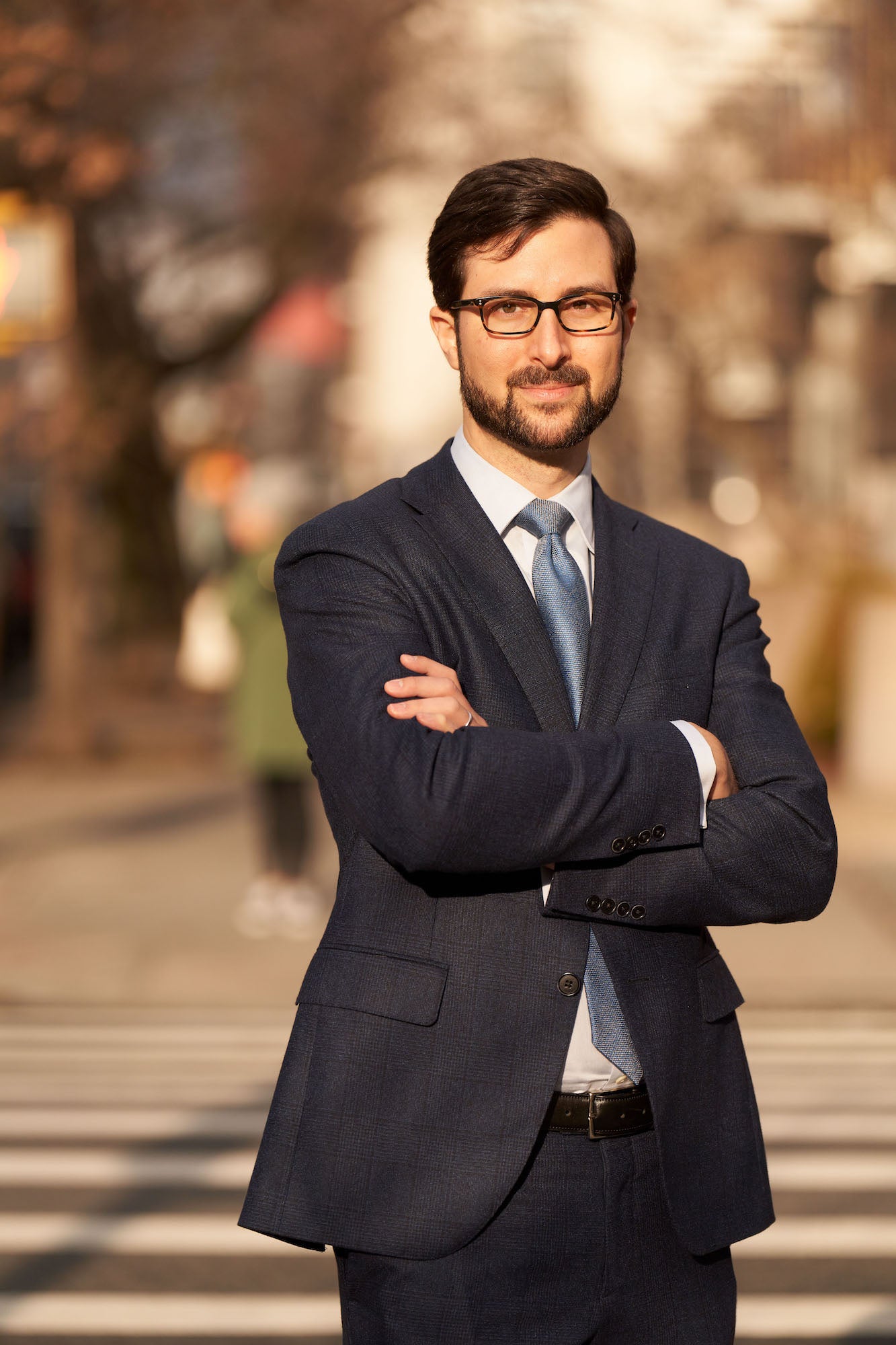 Environmental portrait of a man in a suit with arms crossed, standing outside.