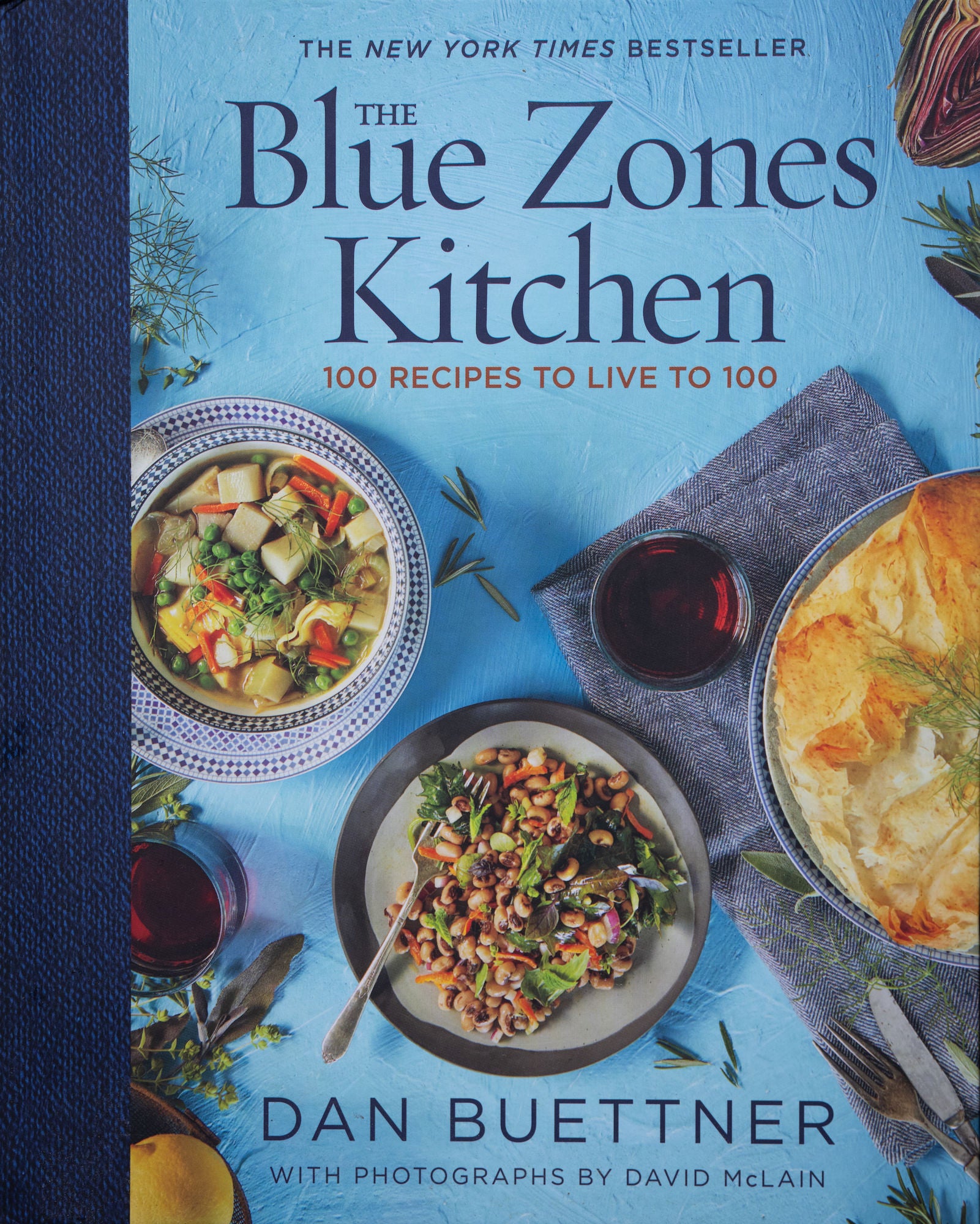 Book cover: “The Blue Zones Kitchen—100 Recipes to Live to 100” by Dan Buettner with overhead dishes. Book cover: “The Blue Zones Kitchen—100 Recipes to Live to 100” by Dan Buettner with overhead dishes.
