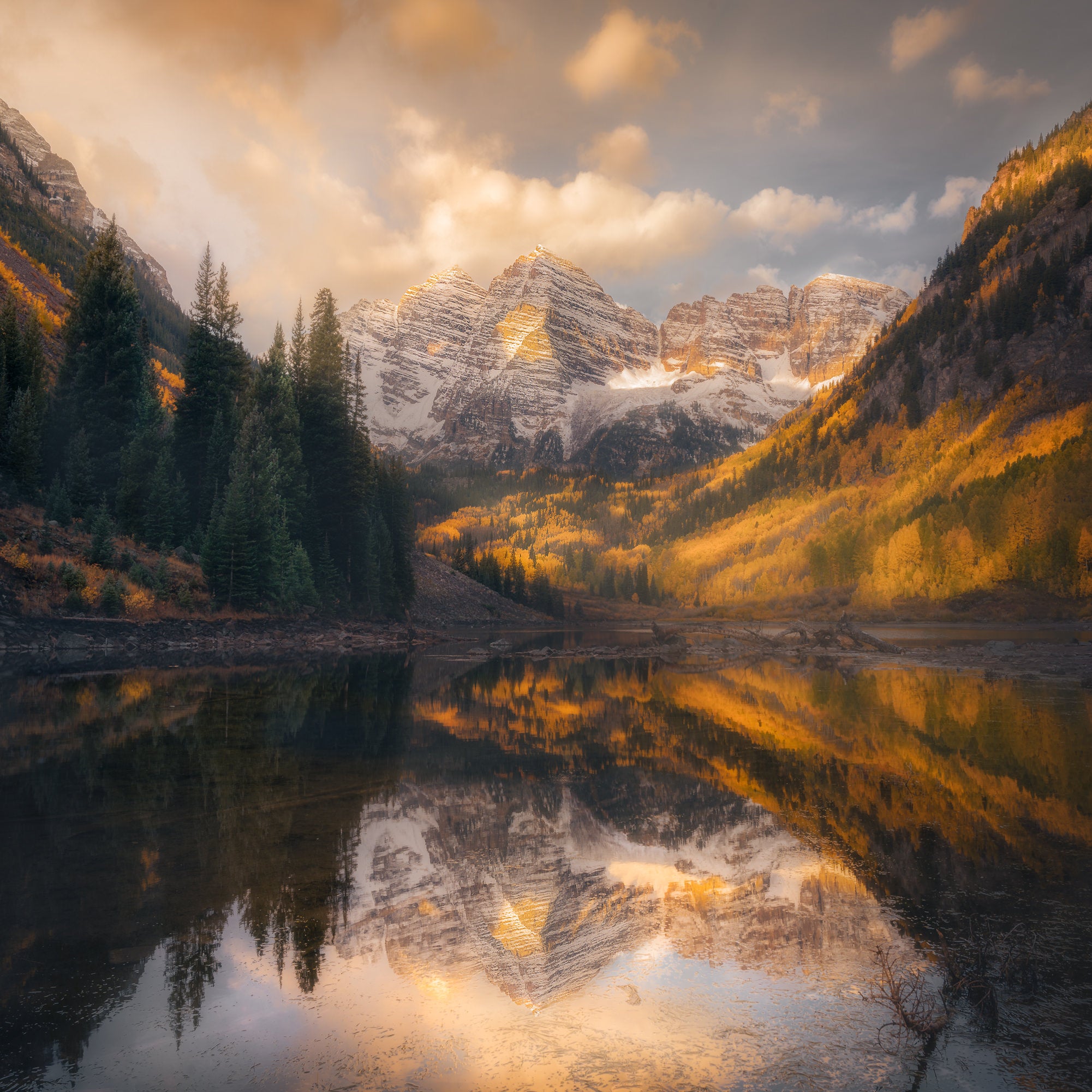 The Maroon Bells glow at sunrise with golden aspens and a mirror-still reflection in Maroon Lake