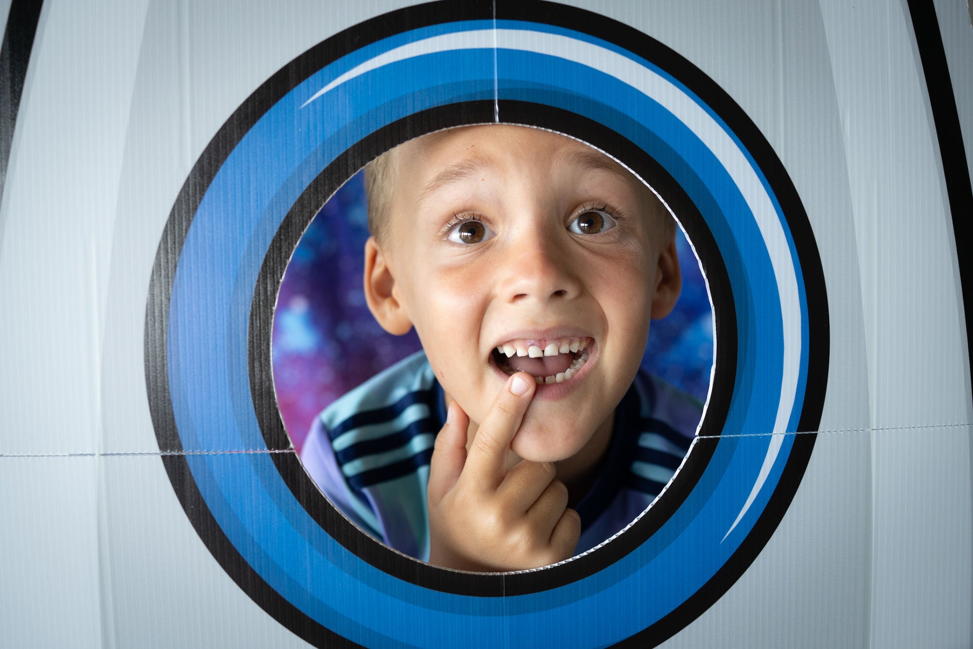 Child in rocket ship photo booth pointing to front tooth