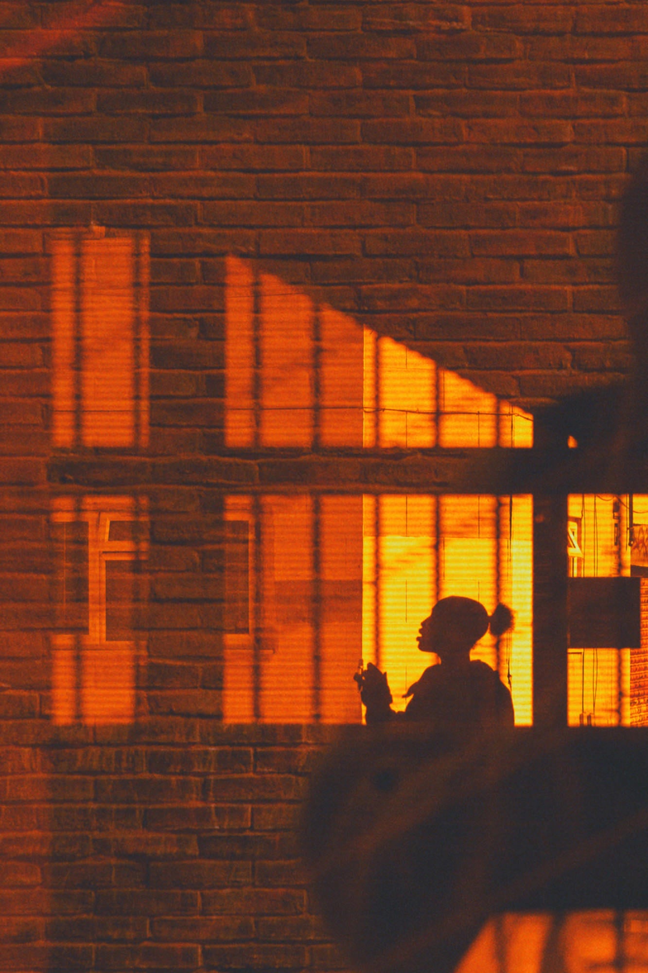 Warm window light casting graphic shadows on brick with a clean silhouette.