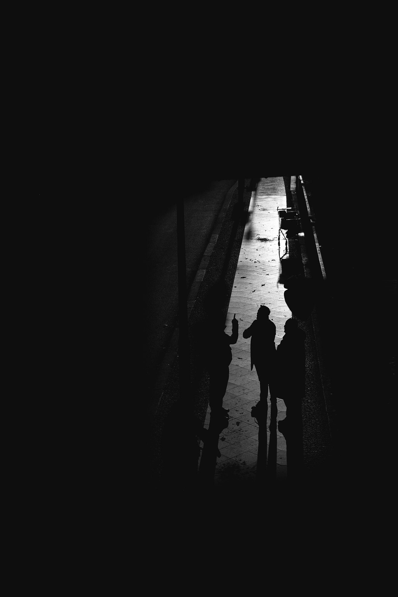 Three silhouettes conversing in a narrow alley, high-contrast black and white.