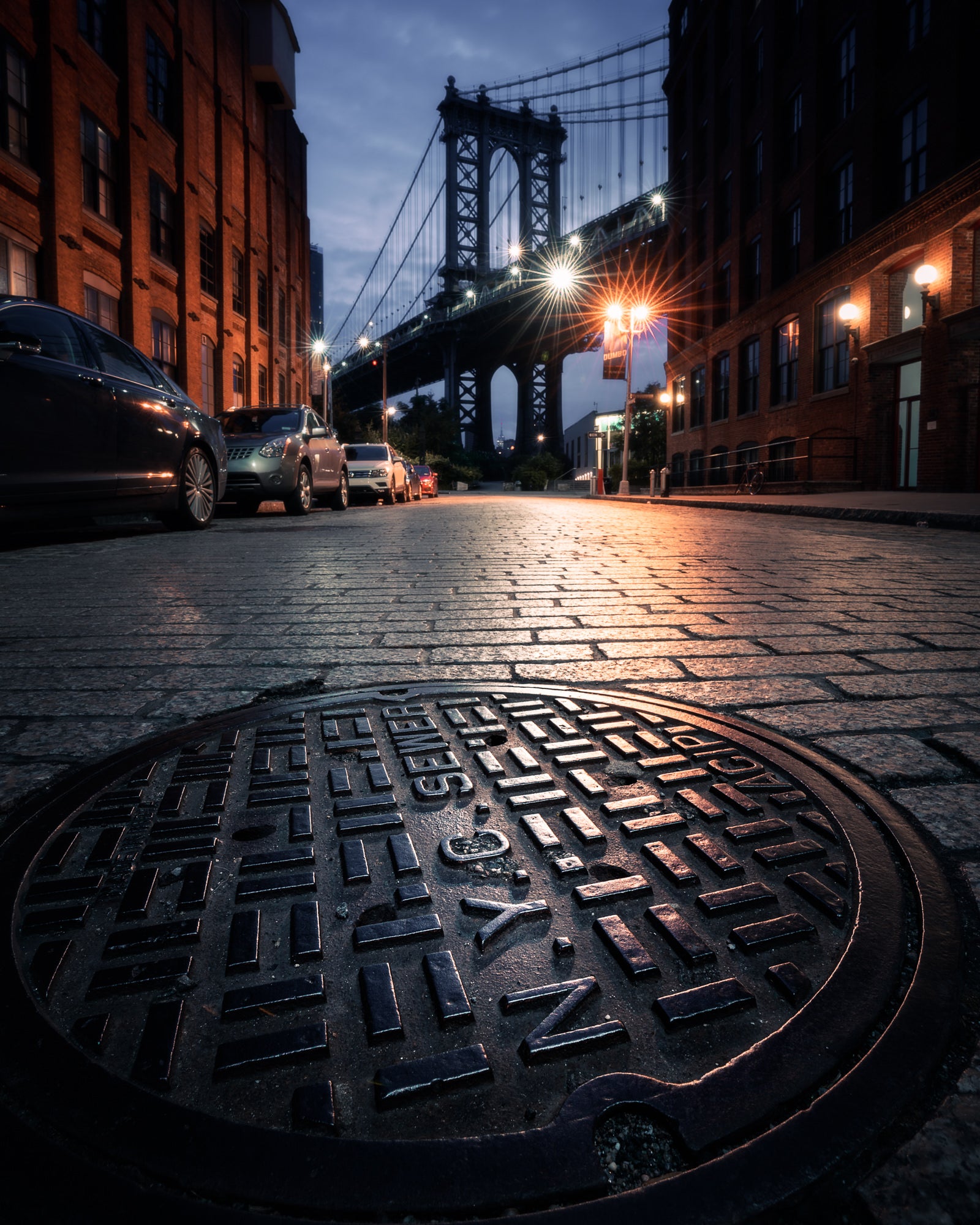 Low-angle cobblestone street view toward the Manhattan Bridge lights in DUMBO, NYC photo by Paul Clark.