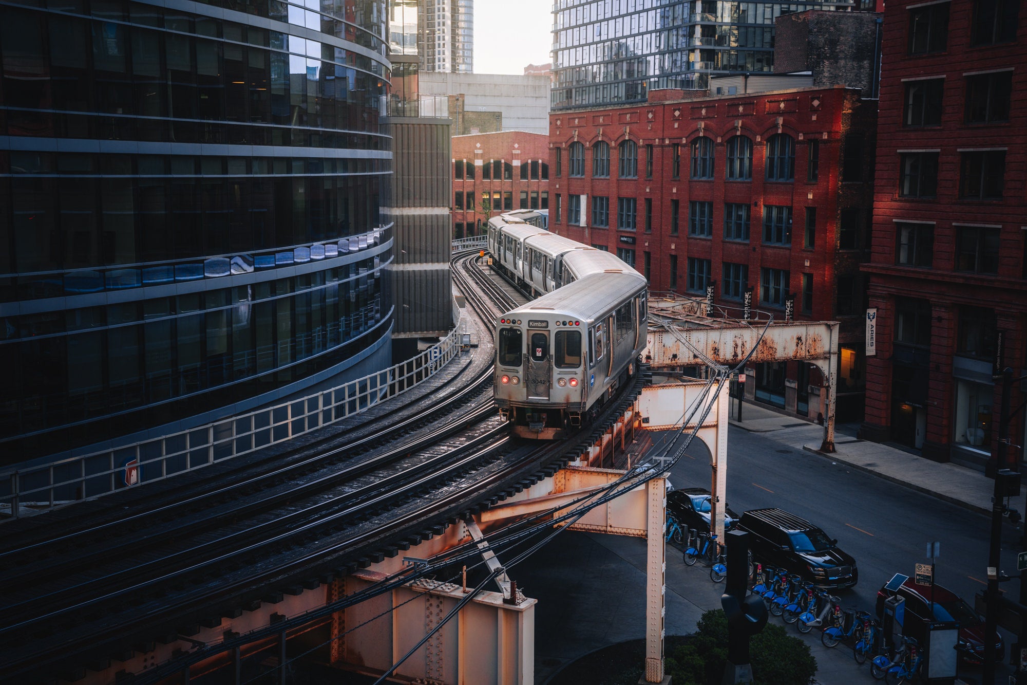 Chicago ‘L’ train navigating curved elevated tracks among red-brick and glass buildings, urban transit image by Paul Clark.