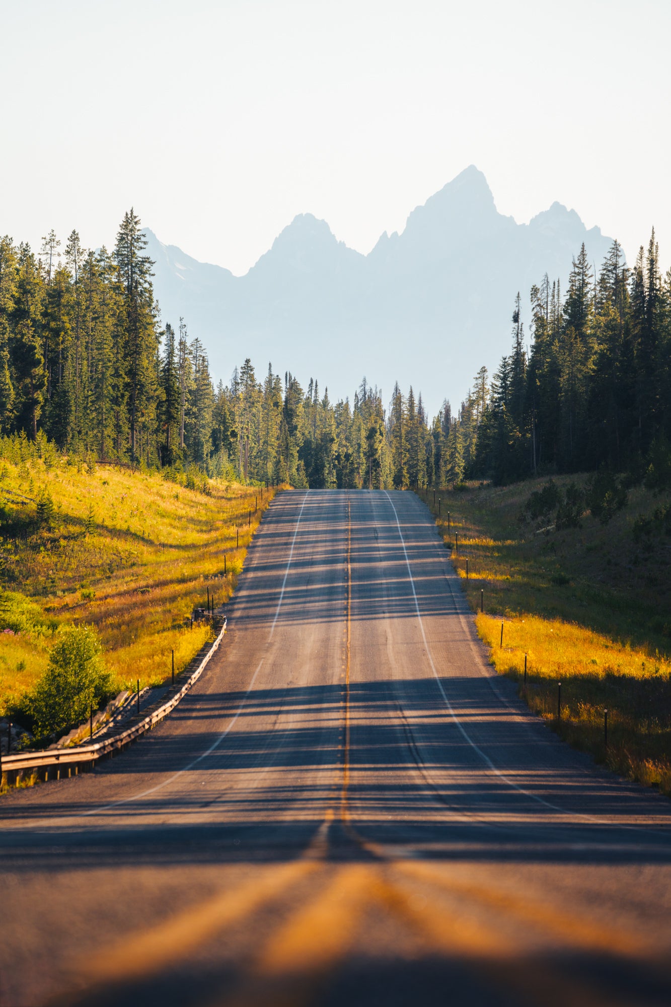 Long road with strong shadows leading to the Teton Range under bright morning sky, Wyoming landscape by Paul Clark.