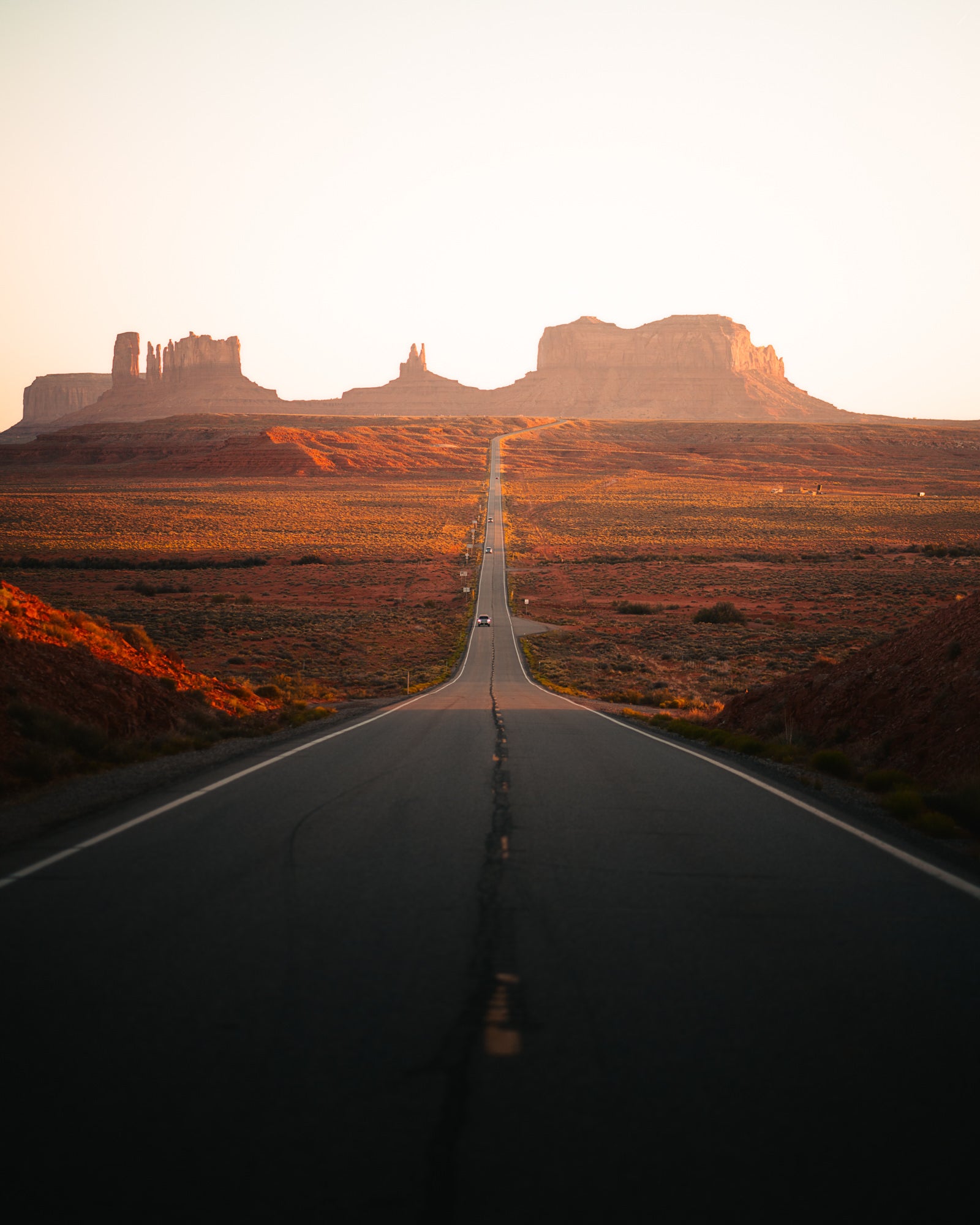 Long straight highway leading into Monument Valley at sunset with red rock buttes, travel landscape by Paul Clark.