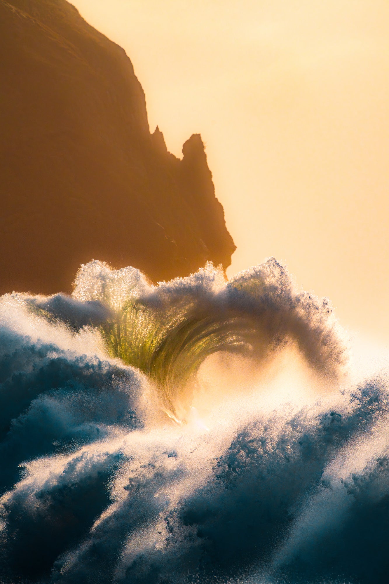 A wave curling and exploding into spray, backlit by golden sunrise light with a dark cliff silhouette behind. Photo by Tomer Negrin. Alpha 7R V. 200-600mm f/5.6-6.3 G OSS. f/11. 1/1600-sec. ISO 250.
