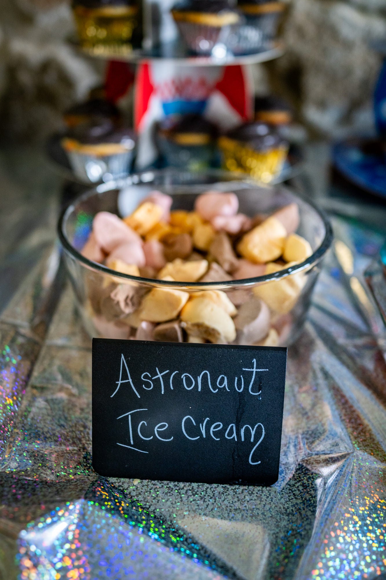 Glass bowl of astronaut ice cream with a chalkboard sign on a sparkly space-themed table.