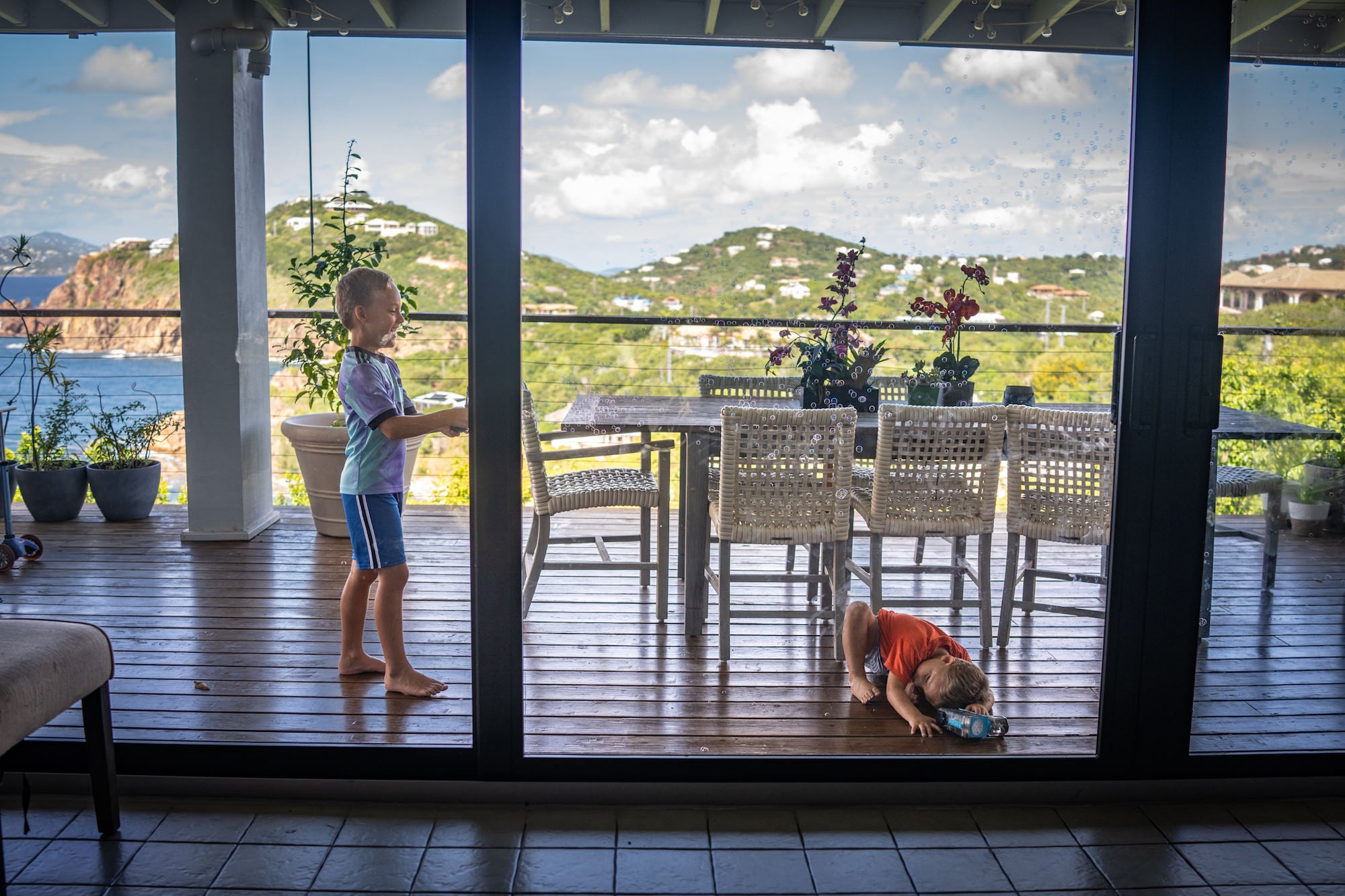 Two young boys on a wooden deck overlooking the ocean and green hills on a sunny day.