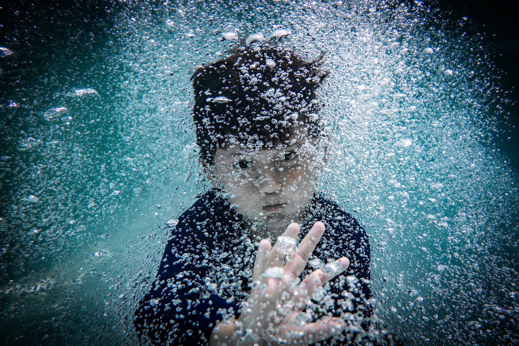 Underwater portrait of a child reaching toward the camera through a cloud of bubbles.