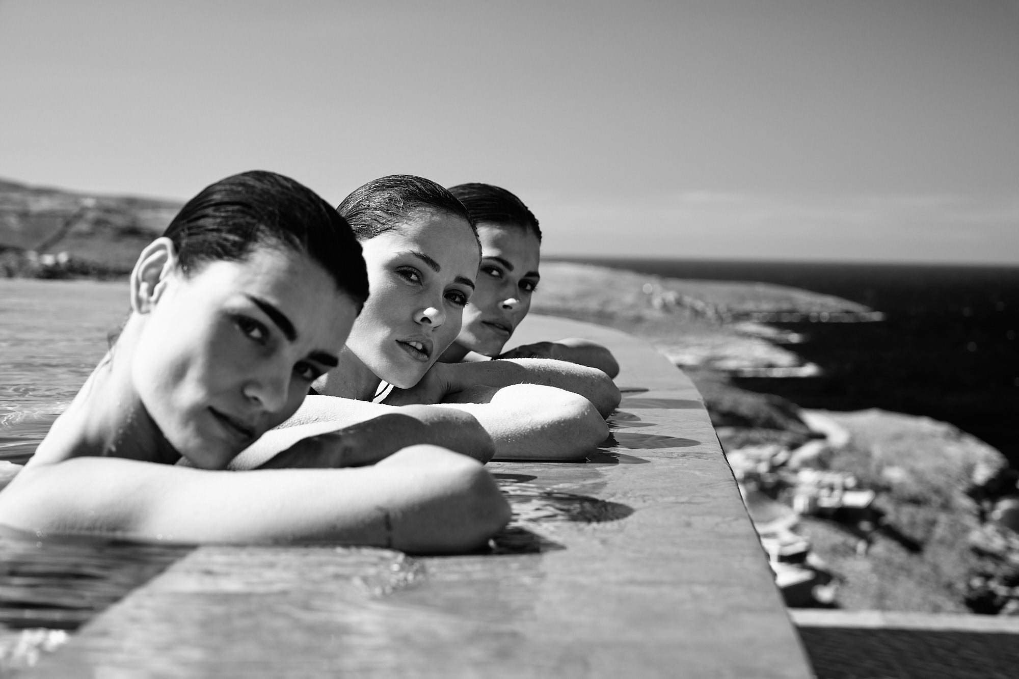 Black and white portrait of three women resting on the edge of an infinity pool overlooking the sea. Black and white portrait of three women resting on the edge of an infinity pool overlooking the sea.