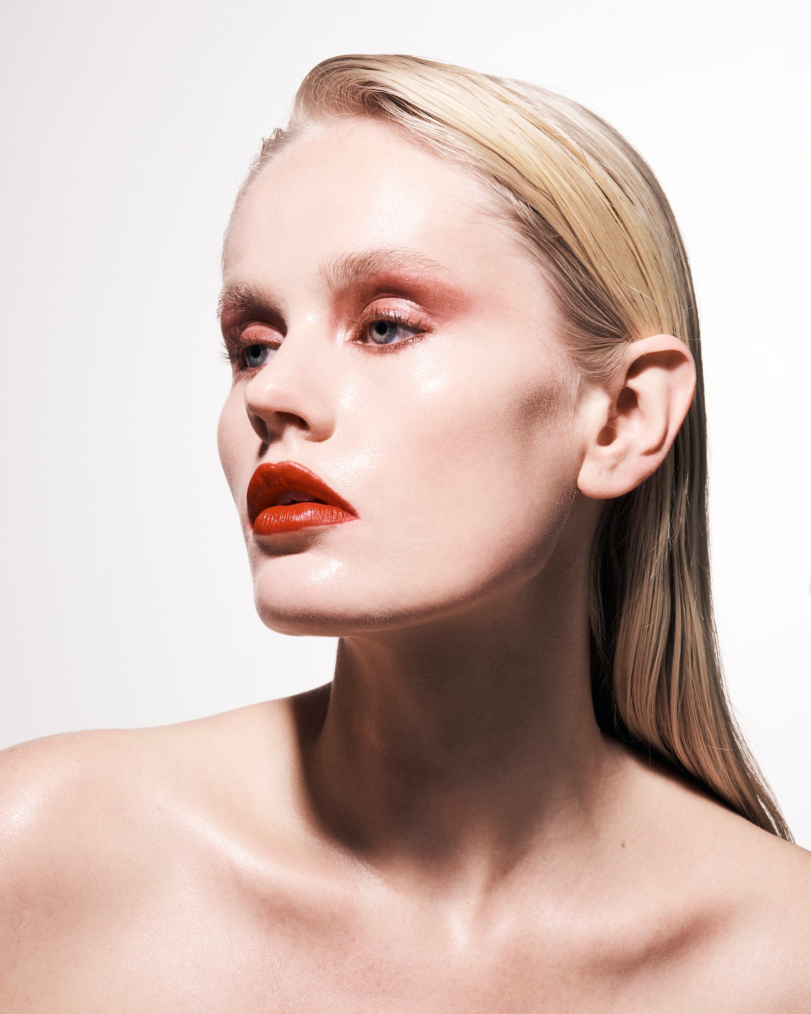 Beauty portrait of a blonde model with slicked-back hair, red lipstick and rosy eye makeup against a white backdrop. Beauty portrait of a blonde model with slicked-back hair, red lipstick and rosy eye makeup against a white backdrop.